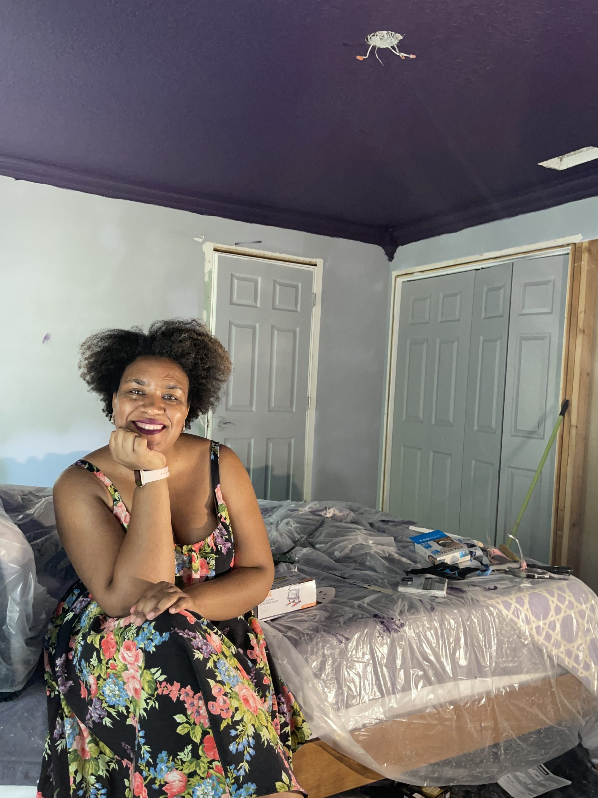 Image of Afro and reno sitting on her bed smiling showing off the new ceiling wearing a pretty floral dress