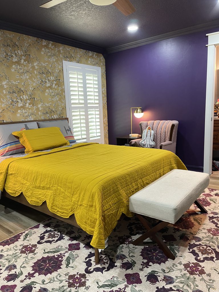 Main bedroom view with the new yellow Van Gogh almond blossom wallpaper, MCM style bed with a yellow scallop quilt, pink chair and purple walls