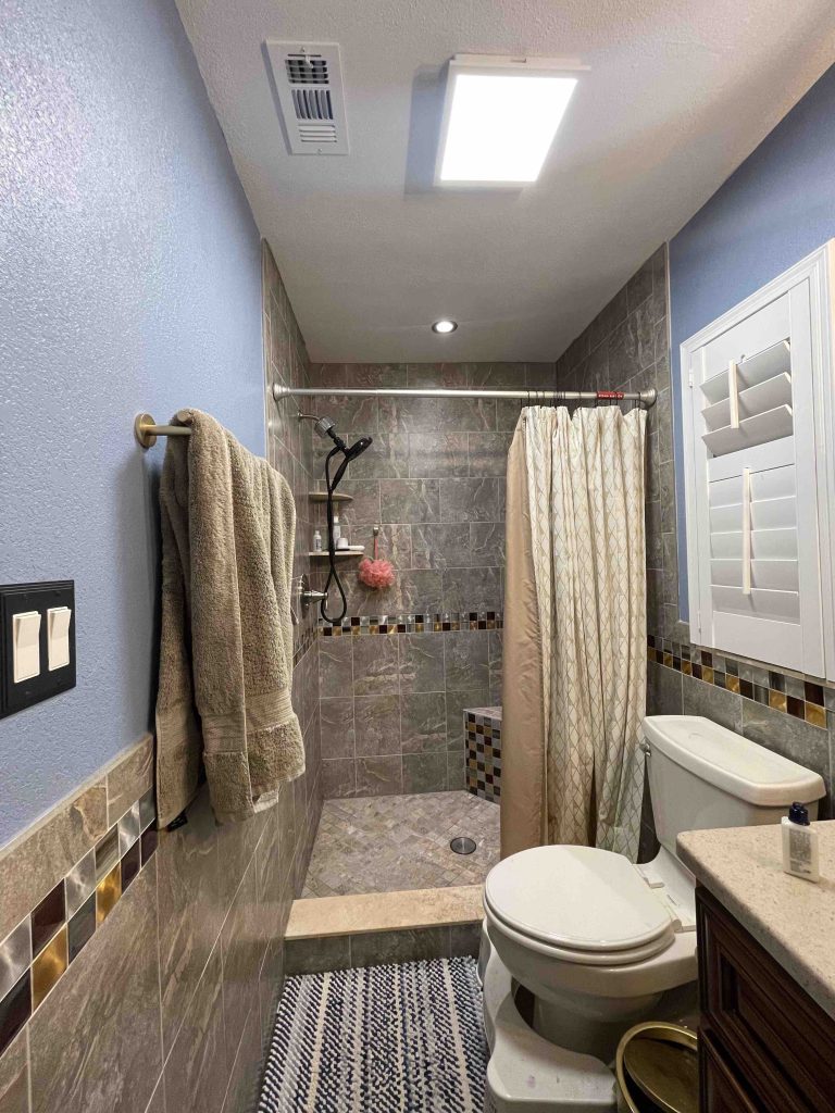 Image of main bathroom before. Showing a gray brown shower with shower curtain. Past the shower the walls are blue and the ceiling is white